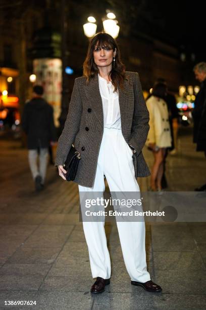 Caroline de Maigret wears gold pendant earrings, a white buttoned high neck shirt, a black and brown houndstooth print pattern blazer coat, a black...