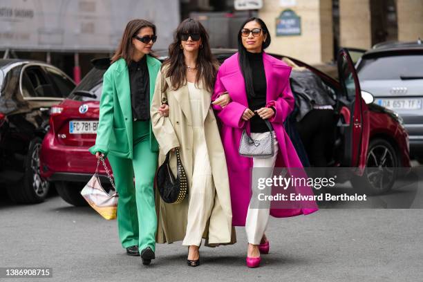 Guest wears black sunglasses, silver earrings, a black shirt, a green blazer jacket, matching green suit pants, a beige / yellow / brown print...