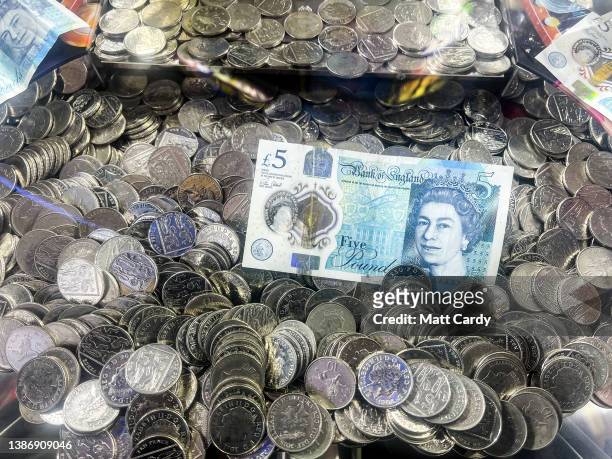 Sterling British Five Pound GBP bank note lies on top of 10p coins that are in an amusement arcade slot machine, on March 20, 2022 in Lyme Regis,...