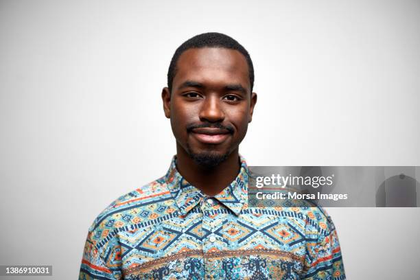 portrait of smiling african businessman. confident young adult male is wearing pattern shirt. he is against white background. - man short hair stock pictures, royalty-free photos & images