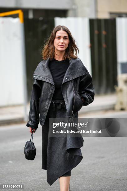 Sophia Roe wears a black pullover, a black shiny leather oversized biker jacket, a dark gray asymmetric midi skirt, a black shiny leather handbag,...