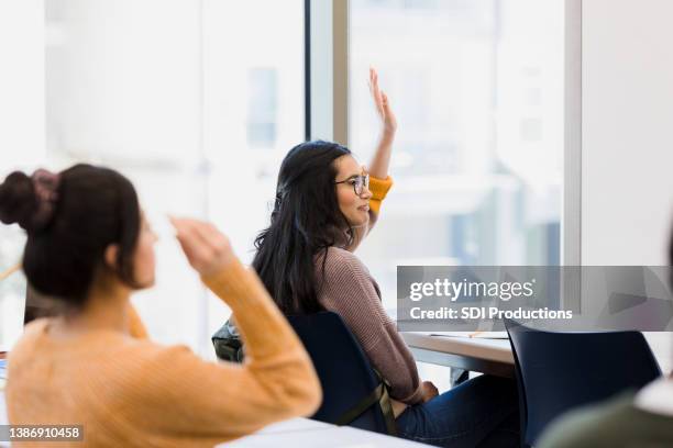 student raises her hand to answer the question - questions answered stock pictures, royalty-free photos & images