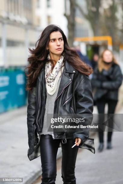 Chiara Tottire wears a white with small black print pattern polar scarf, a black shiny leather oversized biker jacket, black shiny leather skinny...