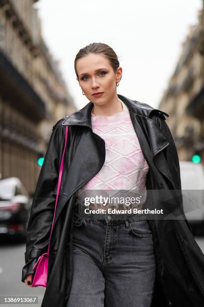 Iana Rad wears silver earrings, a pale pink and white tie and dye braided wool ripped cropped pullover, a black shiny leather long coat, a neon pink...