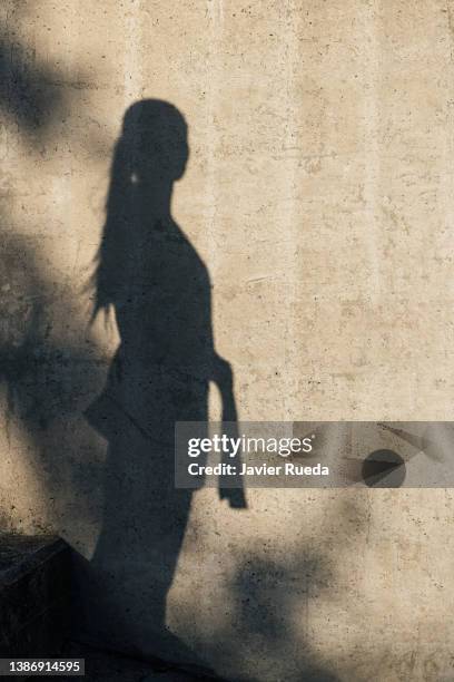 portrait of shadow of strong confident woman with martial arts uniform and black belt projected on a grey concrete wall. silhouette of sporty young athlete doing exercise outdoors and training. - zwarte band stockfoto's en -beelden