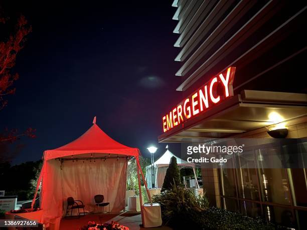 Night view of illuminated red sign for Emergency department or emergency room at a hospital in Walnut Creek, California with isolation tent visible,...