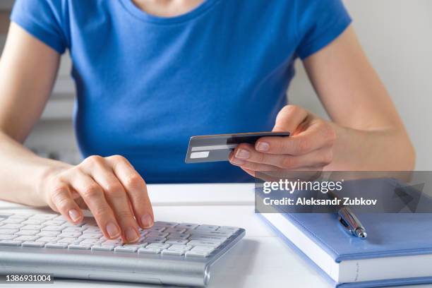 a woman is holding a credit card, typing on a laptop keyboard. there's a notepad and a pen next to it. the concept of buying online, ordering products at home, and paying via the internet. - laptop ban stock pictures, royalty-free photos & images