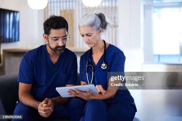 two doctors working together, looking at digital tablet - medizinische dokumente stock-fotos und bilder