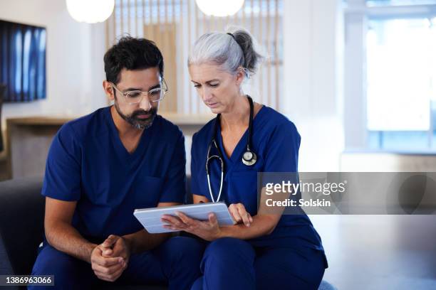 two doctors working together, looking at digital tablet - two doctors talking stockfoto's en -beelden