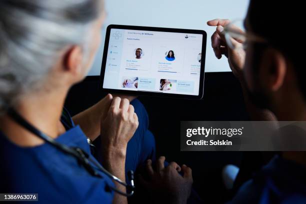 two doctors looking at patient data on digital tablet - krankenakte stock-fotos und bilder