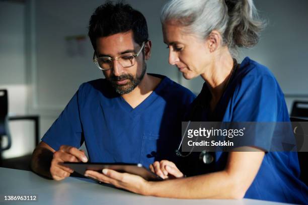 two doctors working together looking at digital tablet - two doctors talking stockfoto's en -beelden