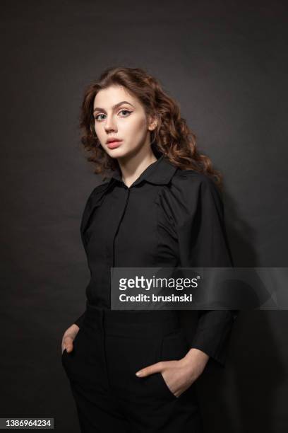 studioporträt einer 20-jährigen frau mit lockigem braunem haar in einem schwarzen hemd auf schwarzem hintergrund - 20 year old stock-fotos und bilder