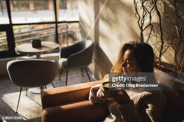 sleepy woman awakening with first morning coffee in cafe. beautiful sun light from window - enjoying coffee cafe morning light stock pictures, royalty-free photos & images