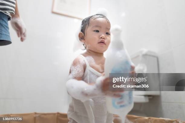 asian baby holding shower gel bottle and playing with foam in bathroom with mother - bubble bath bottle stock pictures, royalty-free photos & images