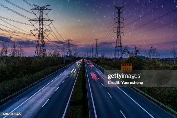 high angle view of electric pylons and light trails on road during beautiful sunset - power grid stock-fotos und bilder