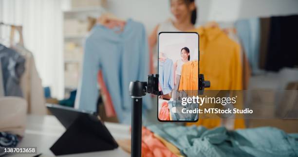 asian businesswoman live-streamed ecommerce sell clothes at home, beautiful girl using the smartphone and tablet for recording video. - for sale bildbanksfoton och bilder