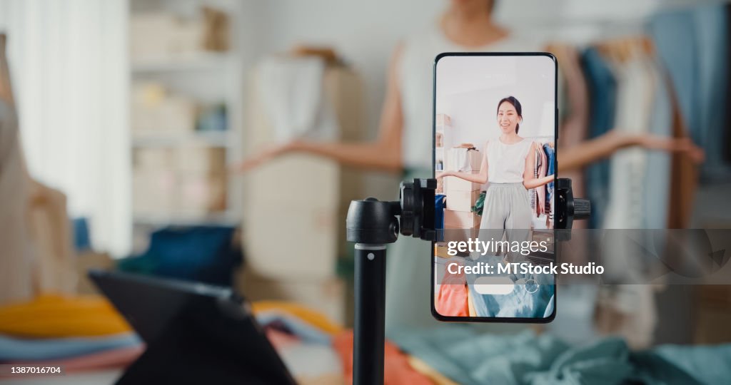 Donna d'affari asiatica in diretta streaming e-commerce vendere vestiti a casa, bella ragazza che utilizza lo smartphone e il tablet per la registrazione di video.