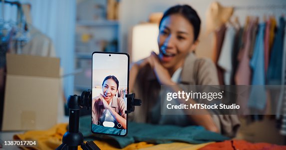 Asian businesswoman live-streamed ecommerce sell clothes in home at night. Beautiful girl using the smartphone and tablet for recording video. Asian businesswoman live-streamed ecommerce sell clothes in home at night. Beautiful girl using the smartphone and tablet for recording video.