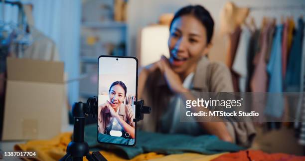 asian businesswoman live-streamed ecommerce sell clothes in home at night. beautiful girl using the smartphone and tablet for recording video. - media interview stock pictures, royalty-free photos & images