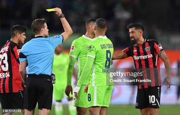 Referee Felix Brych shows the yellow card to Kerem Demirbay of Leverkusen during the Bundesliga match between VfL Wolfsburg and Bayer 04 Leverkusen...