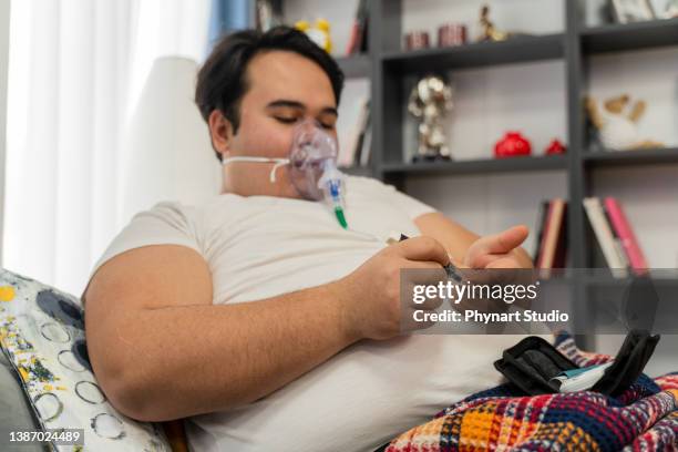 young man sits in a sofa with an oxygen mask and  measuring blood sugar level - obese man stock pictures, royalty-free photos & images