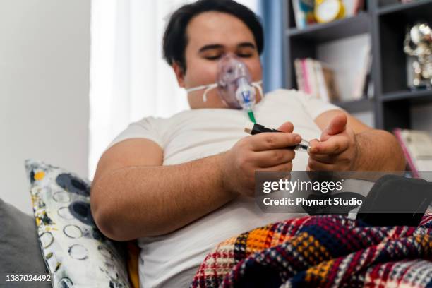 young man sits in a sofa with an oxygen mask and  measuring blood sugar level - obesity imagens e fotografias de stock