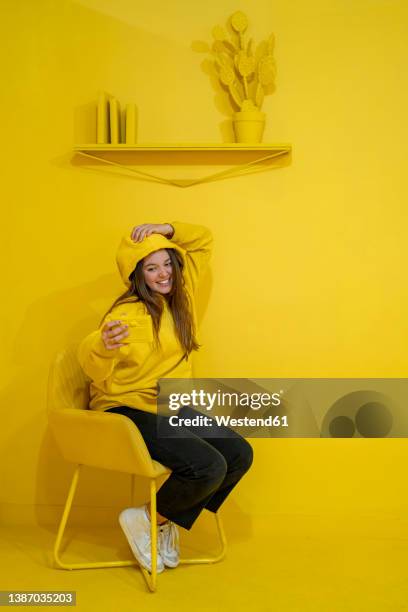 young woman taking selfie on smart phone sitting by yellow background - sitting and using smartphone studio stock pictures, royalty-free photos & images