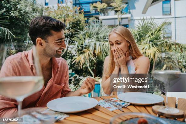 surprised woman looking at man with engagement ring at outdoor table - prometido relación humana fotografías e imágenes de stock