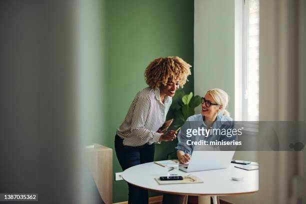 team von zwei glücklichen geschäftsfrauen, die zusammen an einem laptop-computer arbeiten - african lady sitting and looking at her smartphone stock-fotos und bilder