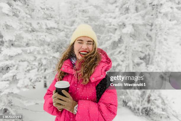 cheerful woman with disposable coffee cup enjoying snowfall - pink coat stock-fotos und bilder