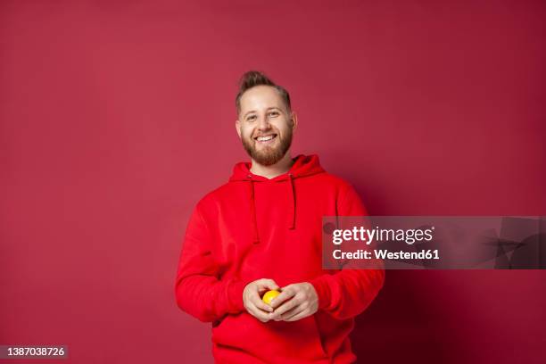 smiling man with lemon against red background - man and his hoodie stockfoto's en -beelden