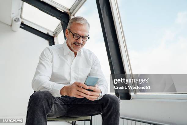 happy businessman text messaging on smart phone at work place - first gray hair stock pictures, royalty-free photos & images