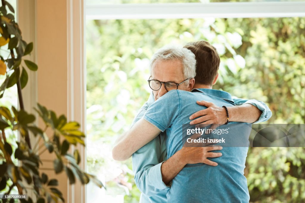 Älterer Mann umarmt Sohn gegen Fenster zu Hause
