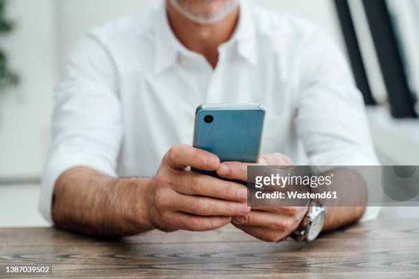businessman text messaging on smart phone at desk in office - middelste deel stockfoto's en -beelden