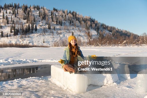 Smiling woman meditating sitting on ice at winter forest