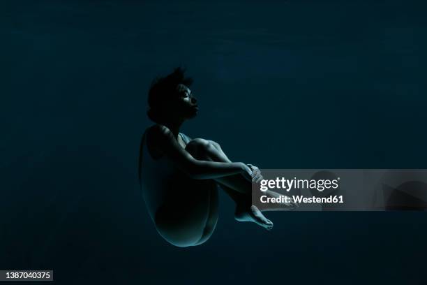 young woman in fetal position swimming underwater - levitation stock-fotos und bilder