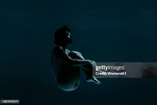 young woman in fetal position swimming underwater - woman underwater stock pictures, royalty-free photos & images