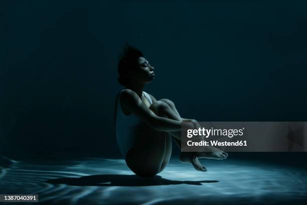 young woman swimming in fetal position undersea - position du foetus photos et images de collection