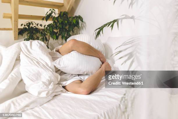 man covering face with pillow lying on bed at home - pillow over head 個照片及圖片檔