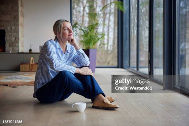 thoughtful woman sitting with hand on chin at home - sentar no chão - fotografias e filmes do acervo