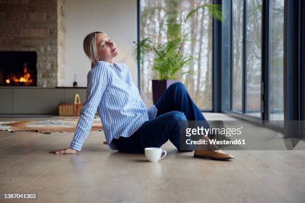 blond woman with eyes closed siting on floor at home - sitting by fireplace stock pictures, royalty-free photos & images