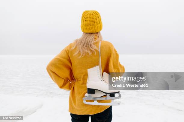 woman in warm clothing standing with ice skates in front of winter sea - ice skating stock pictures, royalty-free photos & images