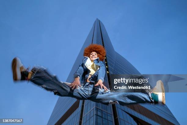 smiling woman in redhead afro hairstyle jumping in front of building at night - legs spread woman stock pictures, royalty-free photos & images