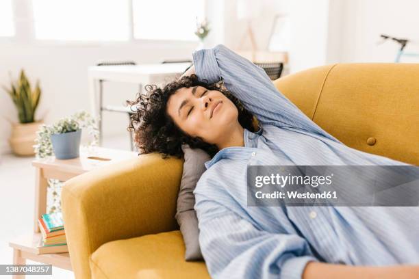 smiling young woman with eyes closed resting on sofa at home - yellow sofa stock pictures, royalty-free photos & images