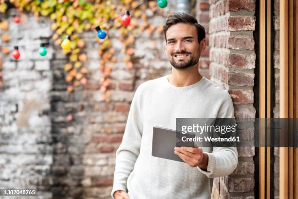 happy freelancer holding tablet pc standing by brick wall - leaning stock pictures, royalty-free photos & images