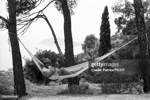 Sacha Distel joue de de la guitare allongé dans un hamac dans le jardin de sa maison à Rayol-Canadel-sur-Mer le 19 juillet 1976