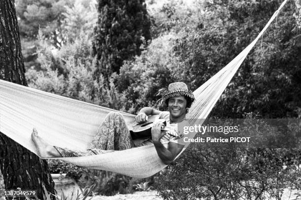 Sacha Distel joue de de la guitare allongé dans un hamac dans le jardin de sa maison à Rayol-Canadel-sur-Mer le 19 juillet 1976