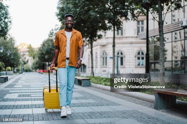 young man walking through the city with suitcase. - yellow suitcase stock pictures, royalty-free photos & images