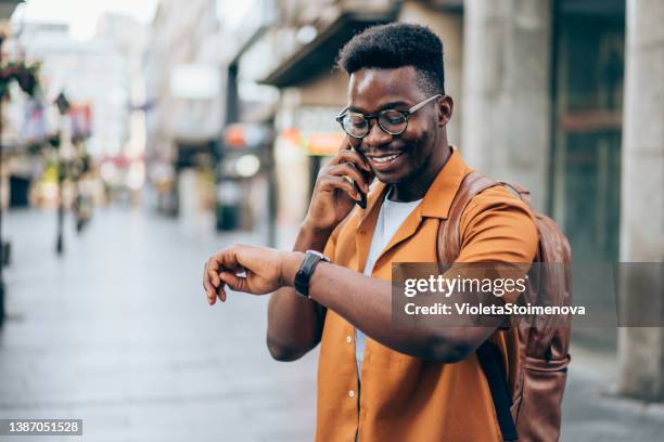 alegre viajero masculino hablando por teléfono móvil en la ciudad. - puntualidad fotografías e imágenes de stock