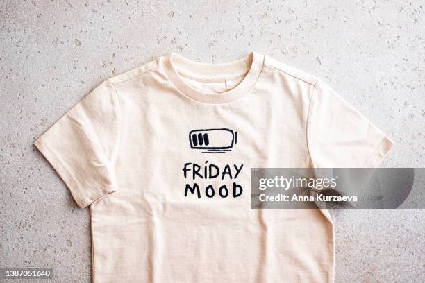 close-up of beige t-shirt with a print “friday mood” on light background, top view - tshirt foto e immagini stock